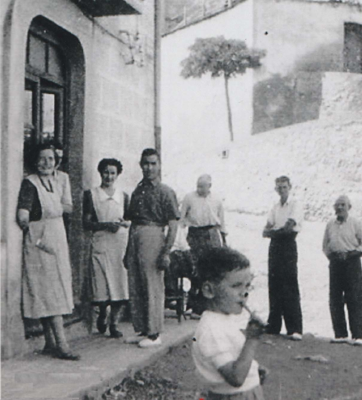 1946 l'Angeleta, la Rosaura i el Jaume del Cantó davant casa seva. El nen podria ser el Tonet del Cantó i dels quatre homes del darrere sols coneixem al Joan (Tano) de cal Rigol i al Quimet de ca la Florinda (vell).jpg