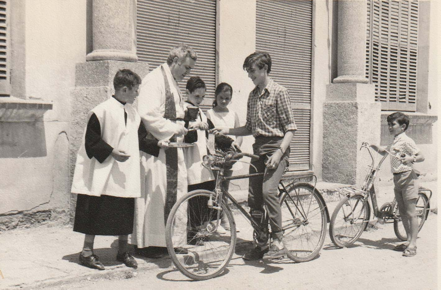 SAN CRISTÒFOL 1968 Mossèn Jaume beneint la bicicleta del Joan de cal Miqueló assistit pels escolans Xavier de cal Miqueló i Josep (Xuri) de cal Jesús.jpg