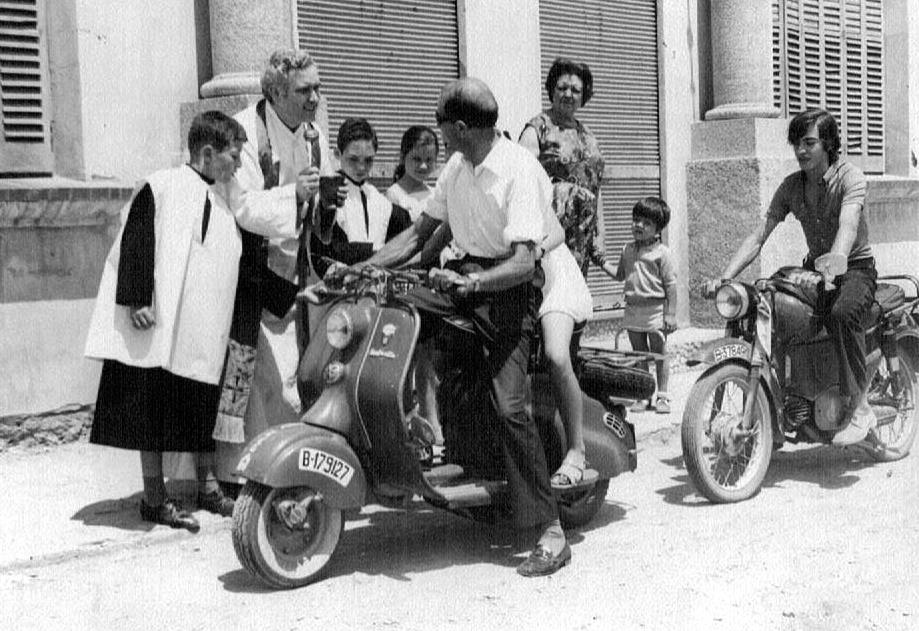 SANT CRISTOFOL. Mossèn Jaume amb els escolanet Josep (Xuri) de cal Jesús i el Xavier de cal Miqueló, beneint les motos del Climent de cal Climent i el Joan de ca la Ció amb la Mercedes de cal Magí al darrere.jpg